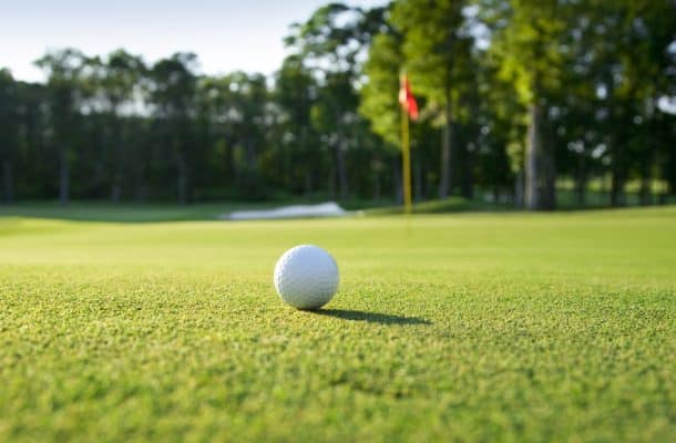 Golf ball sitting on a green with the flagstick nearby